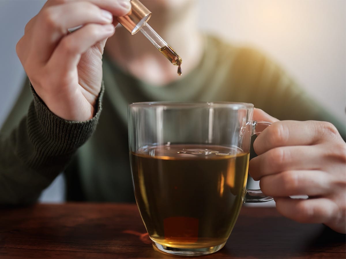 Mão segurando um copo com água e na outra mão a Própolis sendo pingada na água